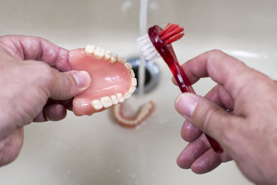 Close up of mans hands carefully cleaning dentures over sink